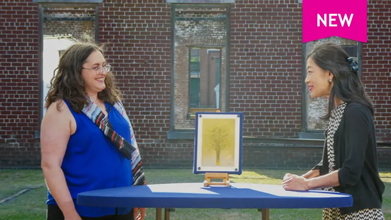 Appraiser Sachiko Hori smiles at a guest as she appraises a print of a tree against a yellow backdrop.