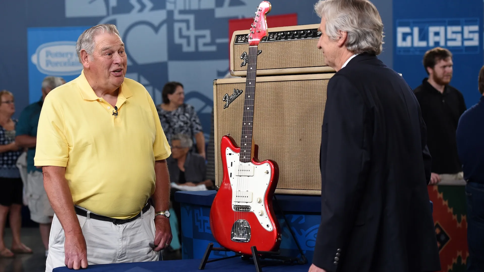 A male guest in a yellow shirt expresses surprise while discussing a Fender Jazzmaster guitar with appraiser Richard Johnston.