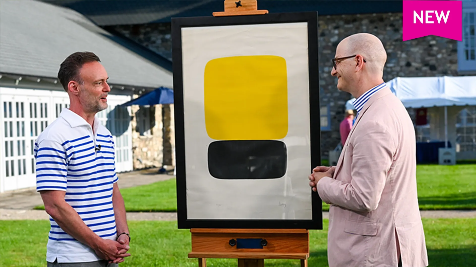 Nigel Freeman speaks with a man about a yellow and black lithograph in front of a brick building and grass