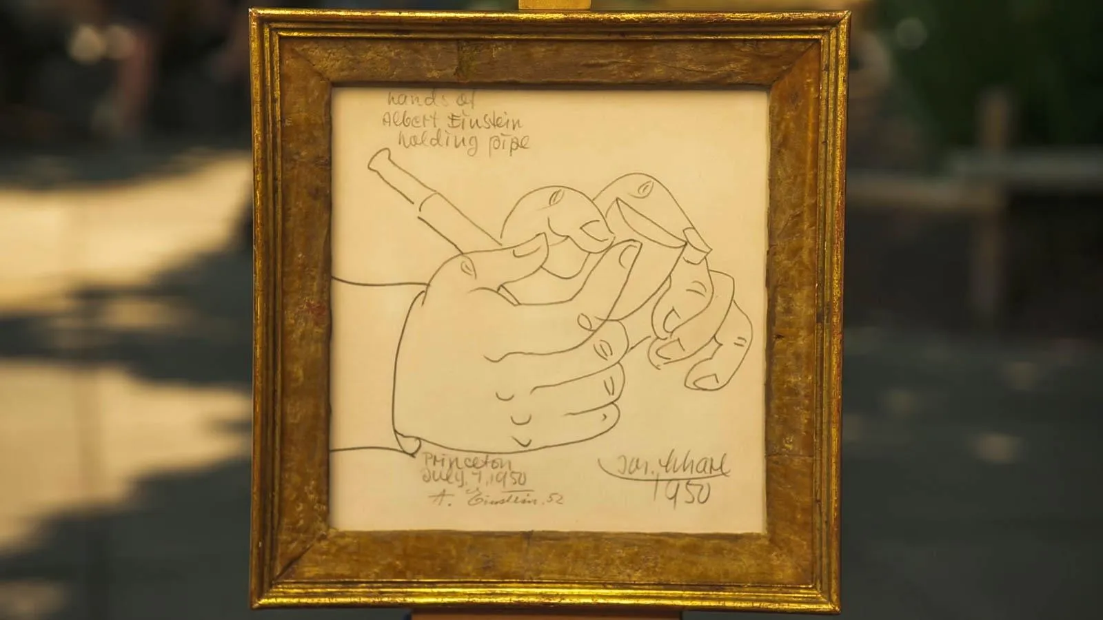Framed sketch of two hands holding a pipe. It is written in the upper-left corner that it is depicting historical figure Albert Einstein's hands. Is signed on the lower right, "Jos. Scharl."