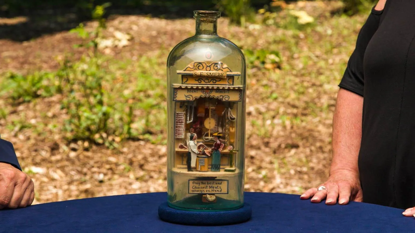 Close up of a glass bottle with a wooden scene of a woman buying meat from a butcher shop