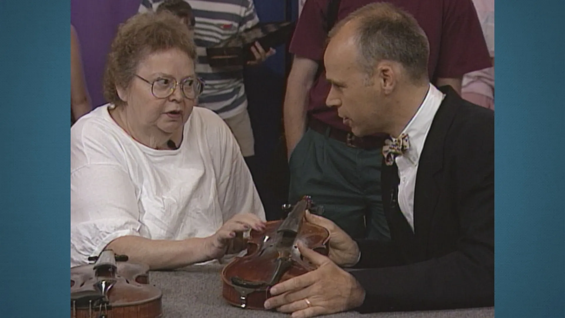 And woman and man, seated at a table, discuss an antique violin.