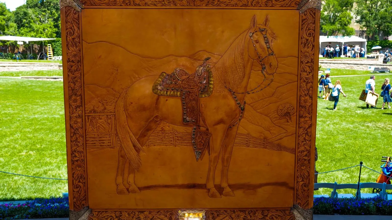 A piece of brown leather with an image of a horse agains some mountains is worked into the material. Along the horse are beaded accents on the reigns and saddle and flowers etched along the edge.