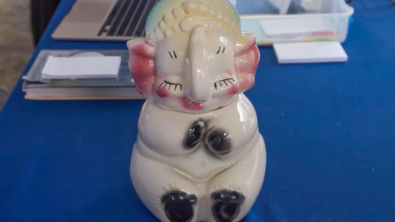 A cream elephant figuring with pink ears and black accents placed on top of blue table