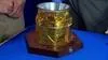 Close up of a cyllindar wrapped in gold foil like fabric on top of a wooden base with metal rim