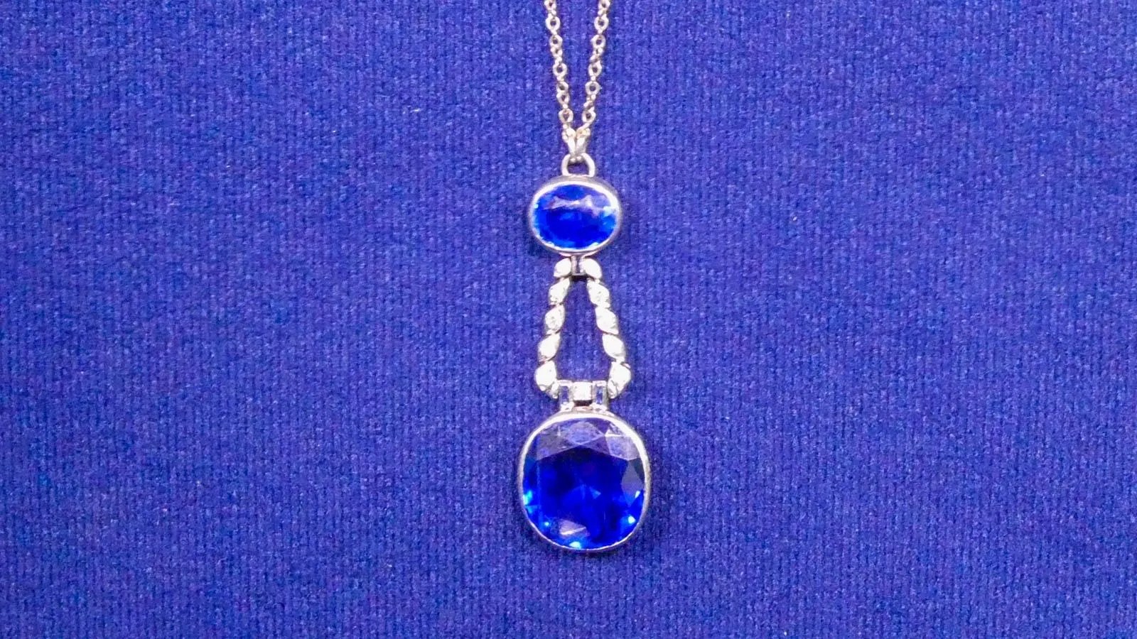 Close up of a silver necklace with two sapphire pendents together making a teardrop shape.
