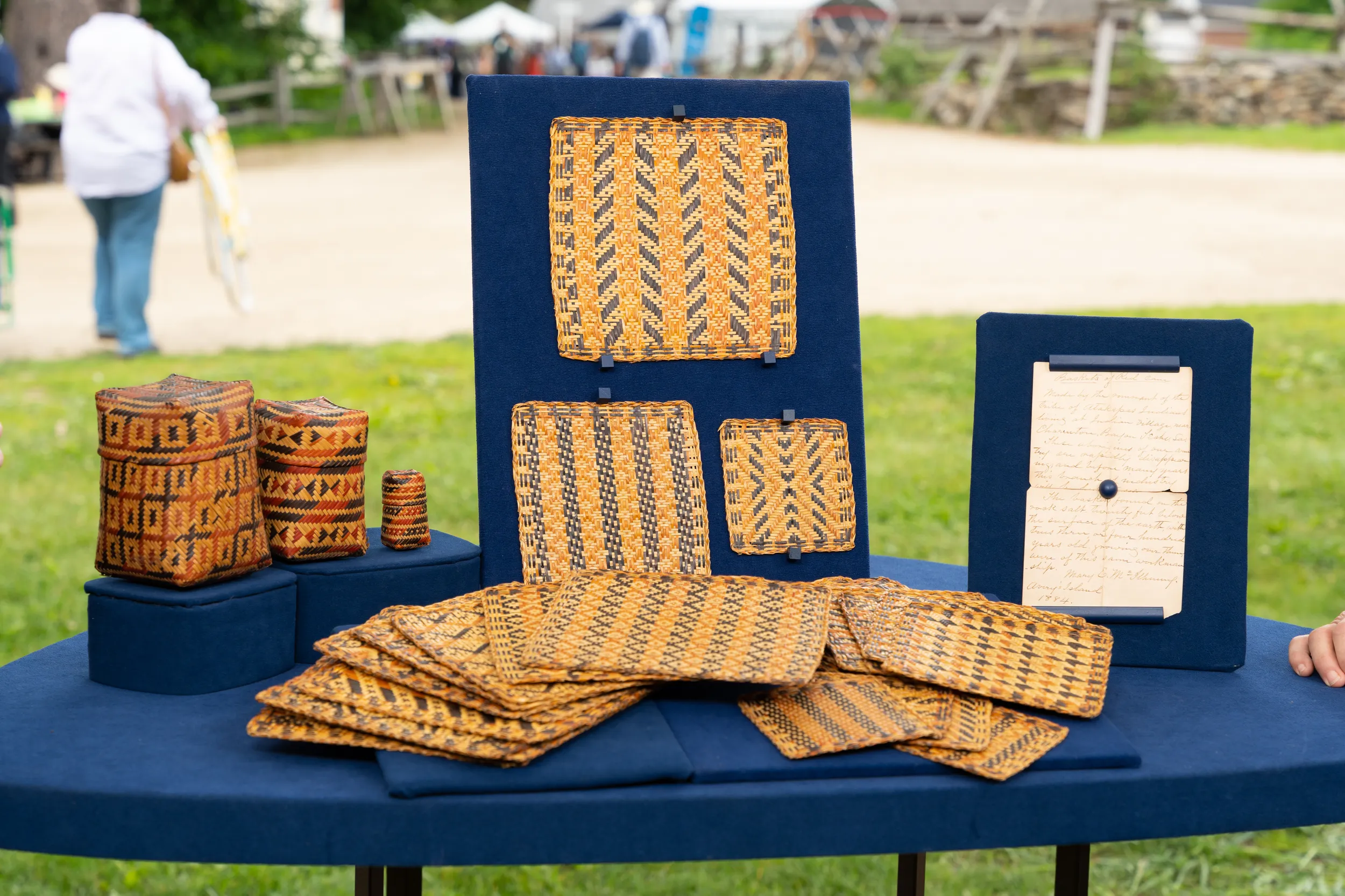 Collection of baskets and placemats on display, along with a handwritten letter on the right. Baskets have geometric pattern design. Placemats have designs interwoven.