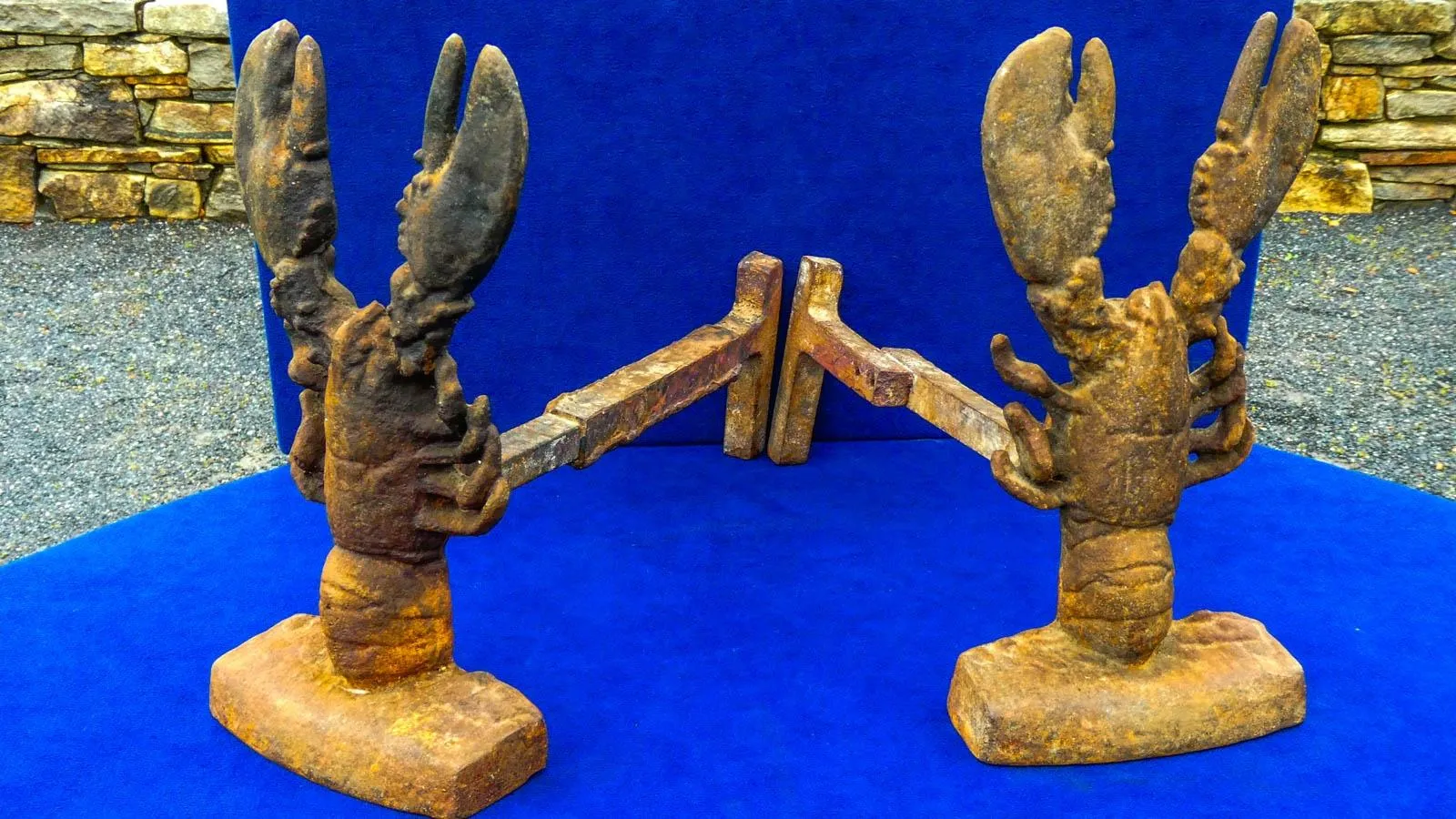 Two rusted lobster andirons against a royal blue background