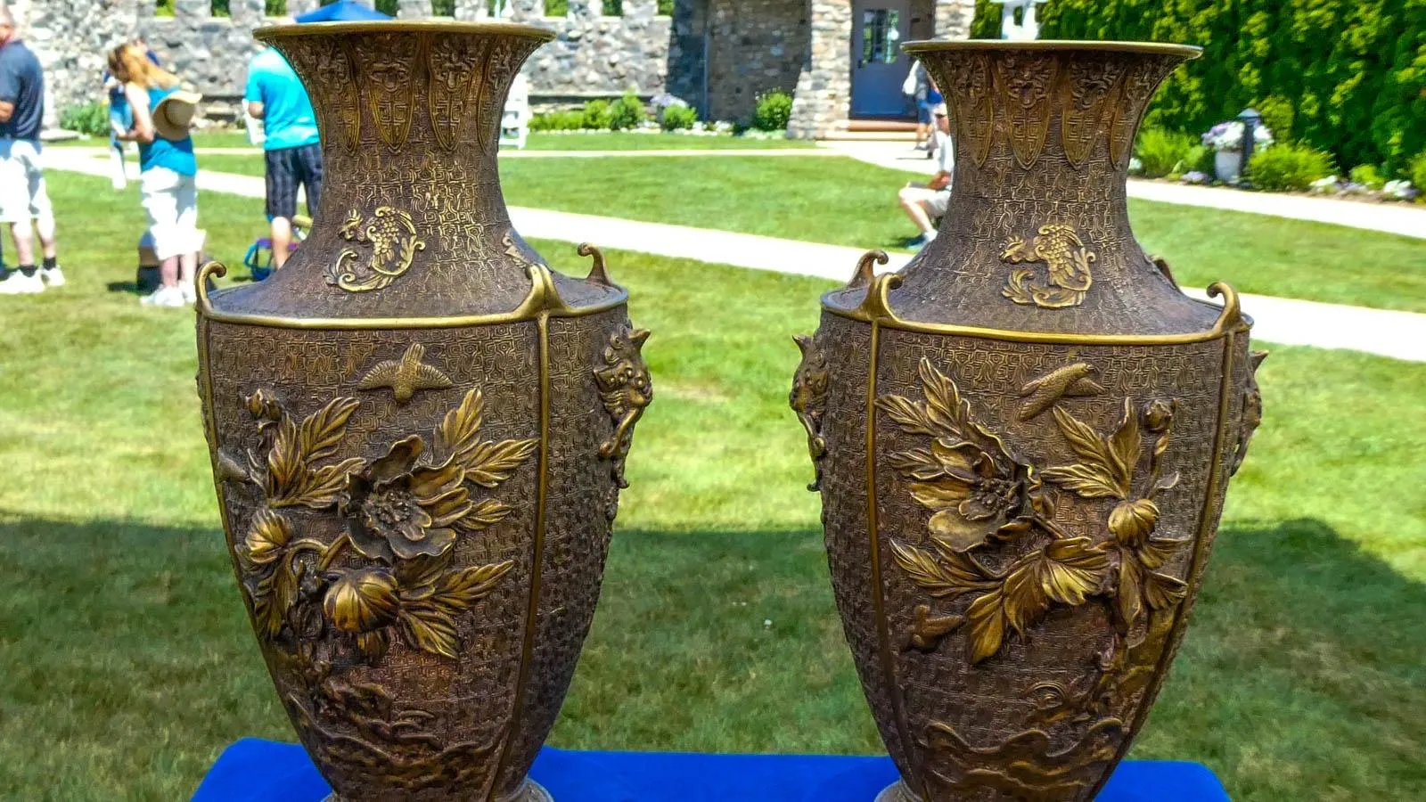 Two bronze color vases with floral details placed on a blue table.
