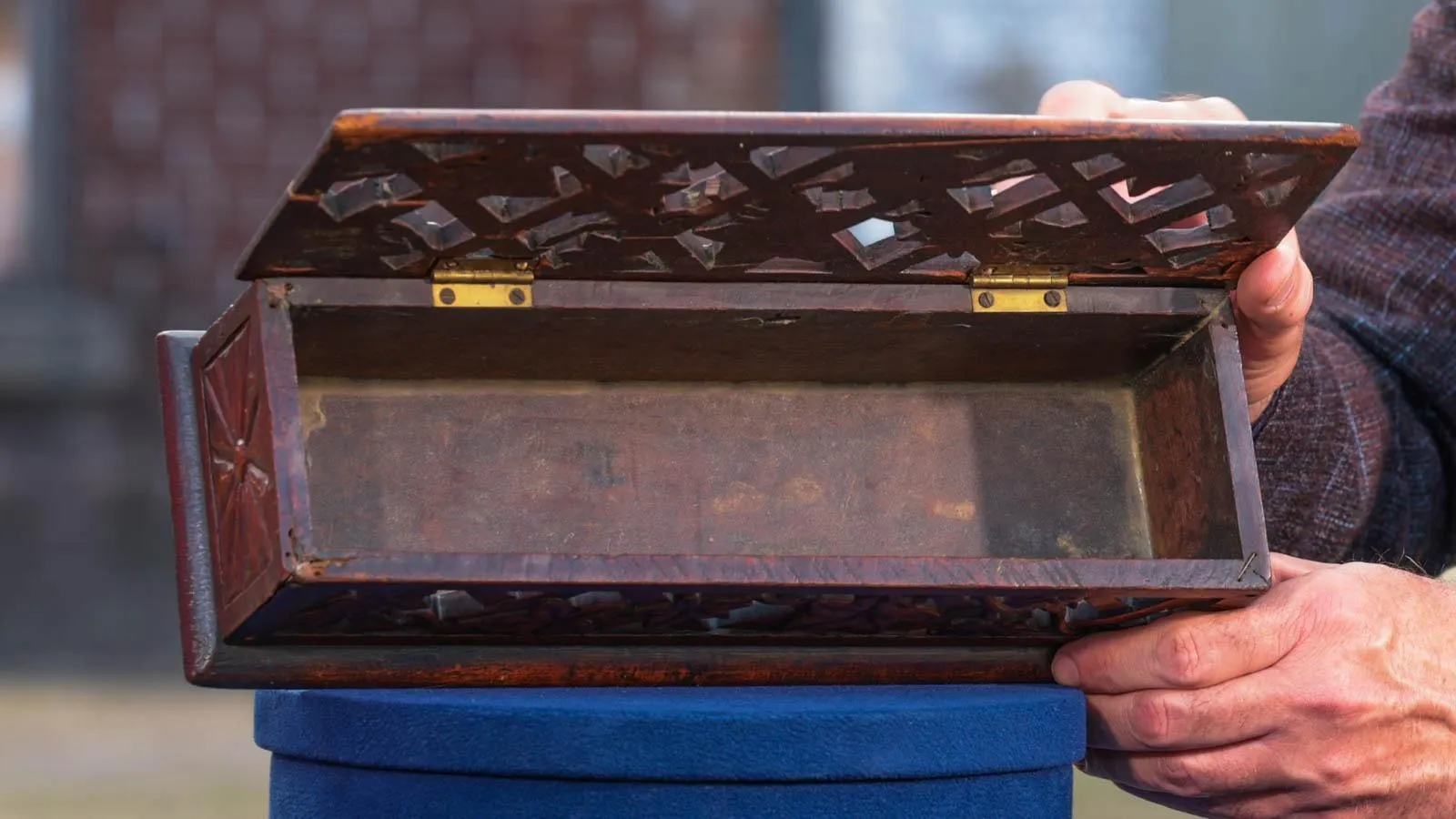 An open wooden box with carved designs on the lid and sides