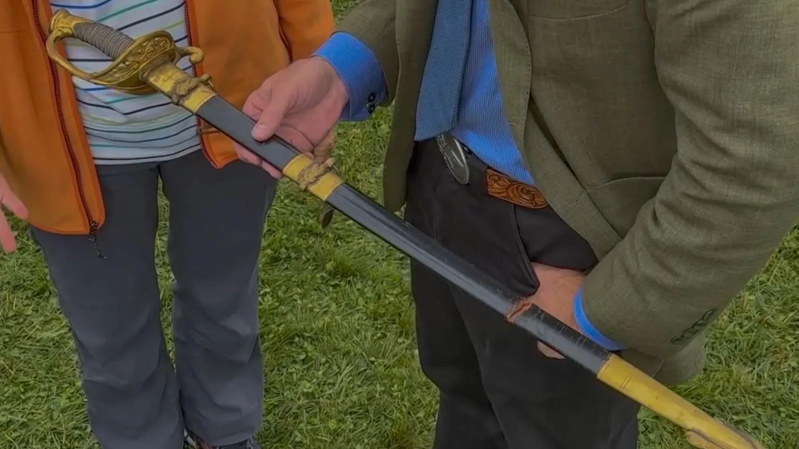 Two people holding a long sword with gold detail.