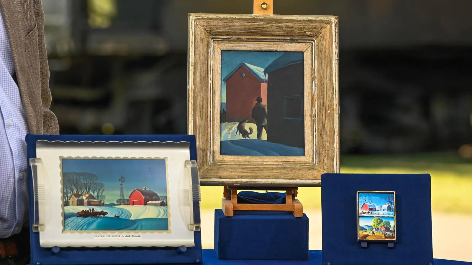 Three small paintings mounted on blue foam board depicting various winter scenes of a red house.