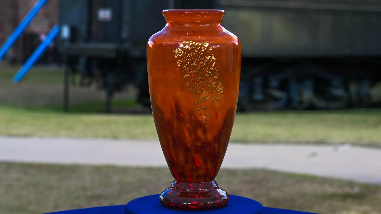 An orange vase with gold accents placed on top of a blue table.