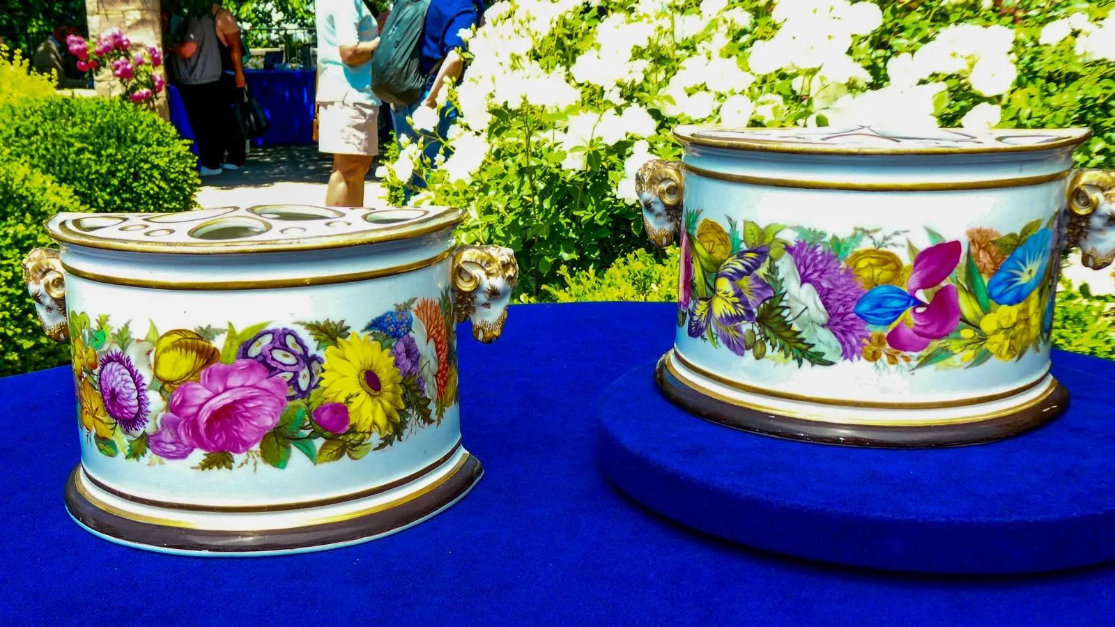 Two white porcelain pots, shaped in half-moons. The pots have gold trimming around the edges with a line of various wildflowers along the side in purple, blue, yellow and orange.