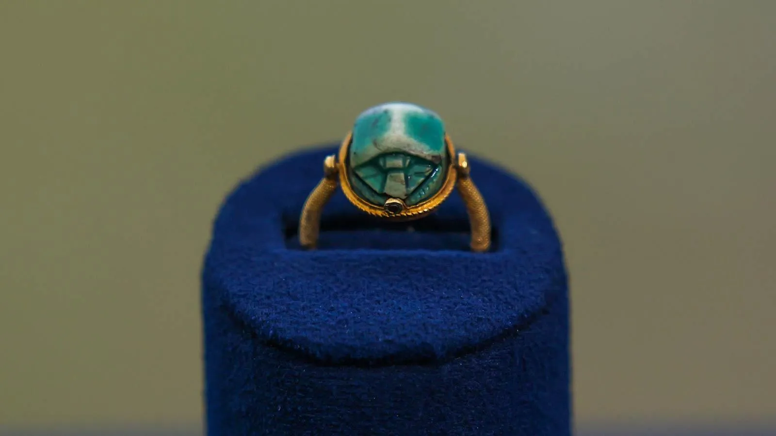 Close image of a gold ring with a teal stone in the center placed in a blue ring holder.