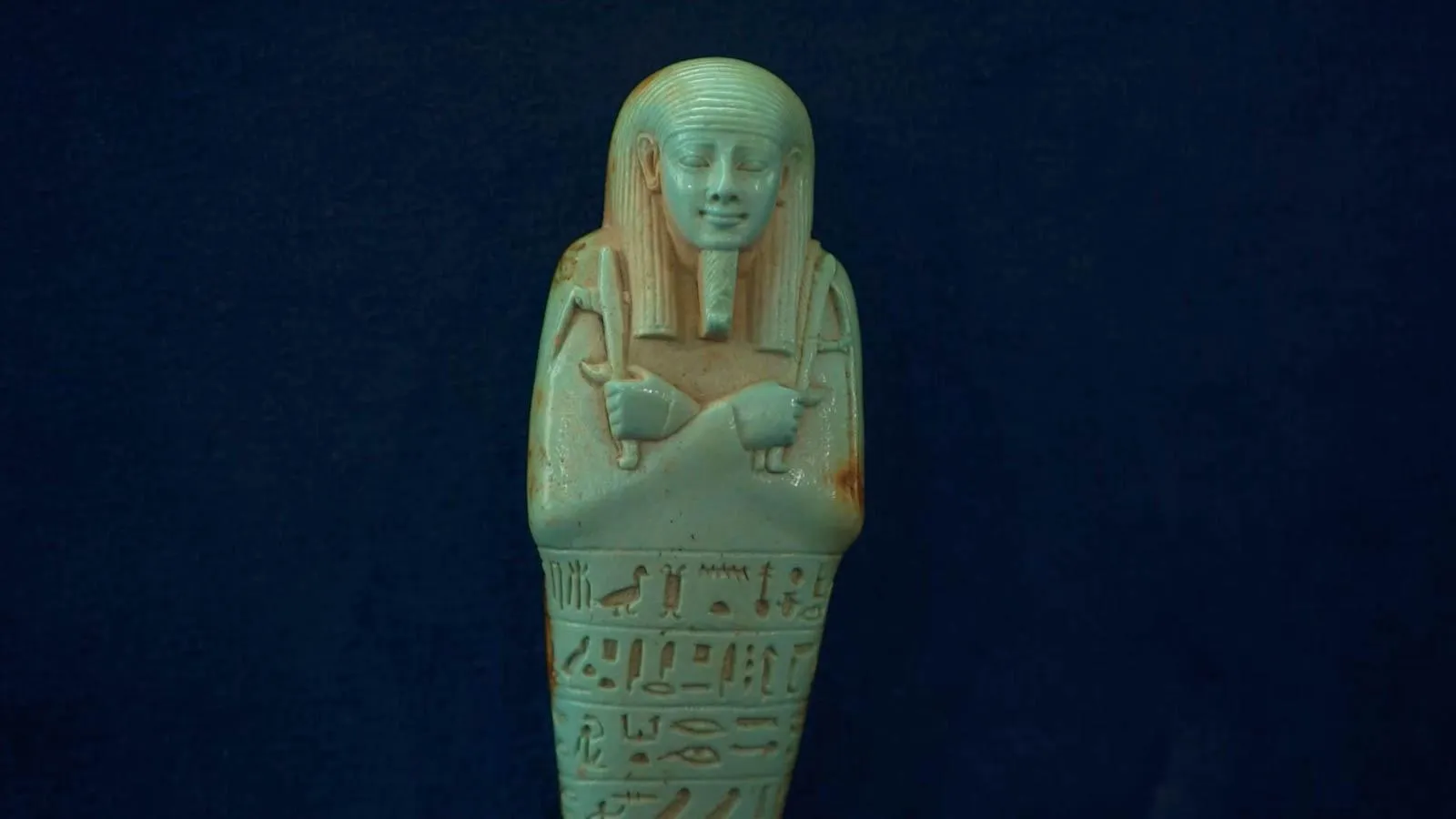 Close up on an off white Egyptian figure against a blue background.