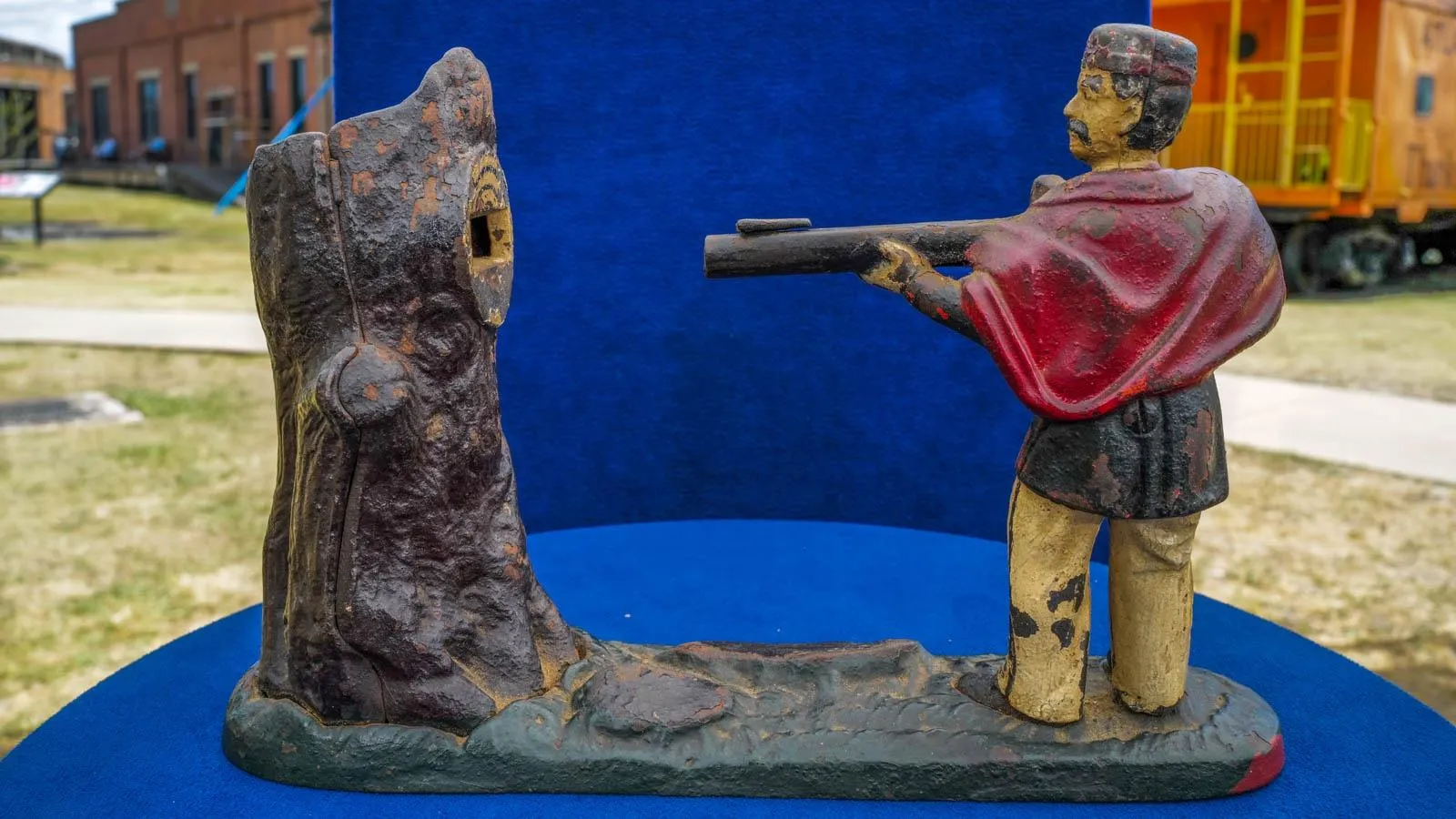 Close up of a toy bank featuring a hunter figure shooting a tree stump with coin slot set against a blue background.