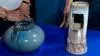 Two vases on a blue table. On the left is a wider blue spherical vase with square handle like accents. On right is Cylindrical white and Mauve vase with rectangle cutouts and mushroom detail on bottom