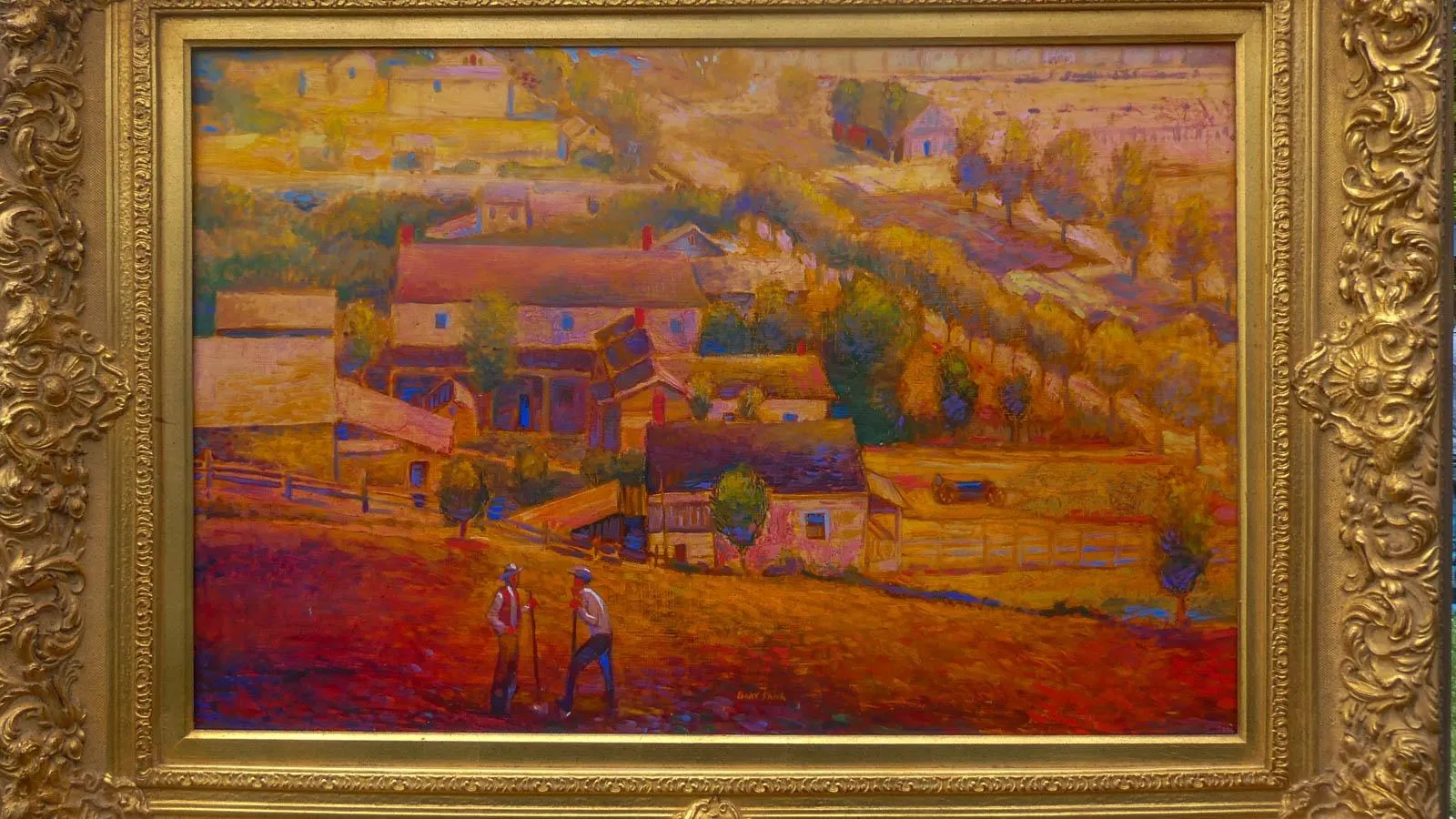 Oil painting in a gold frame. The painting depicts a landscape with houses, trees and farmland in the forefront. Standing on the farmland are two men speaking to one another holding shovels.
