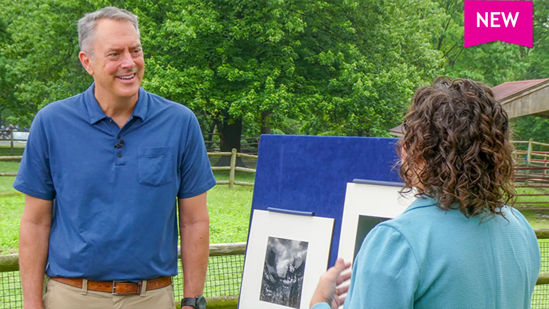 A man smiles while listening to appraiser Deborah Rogal appraise two photographs