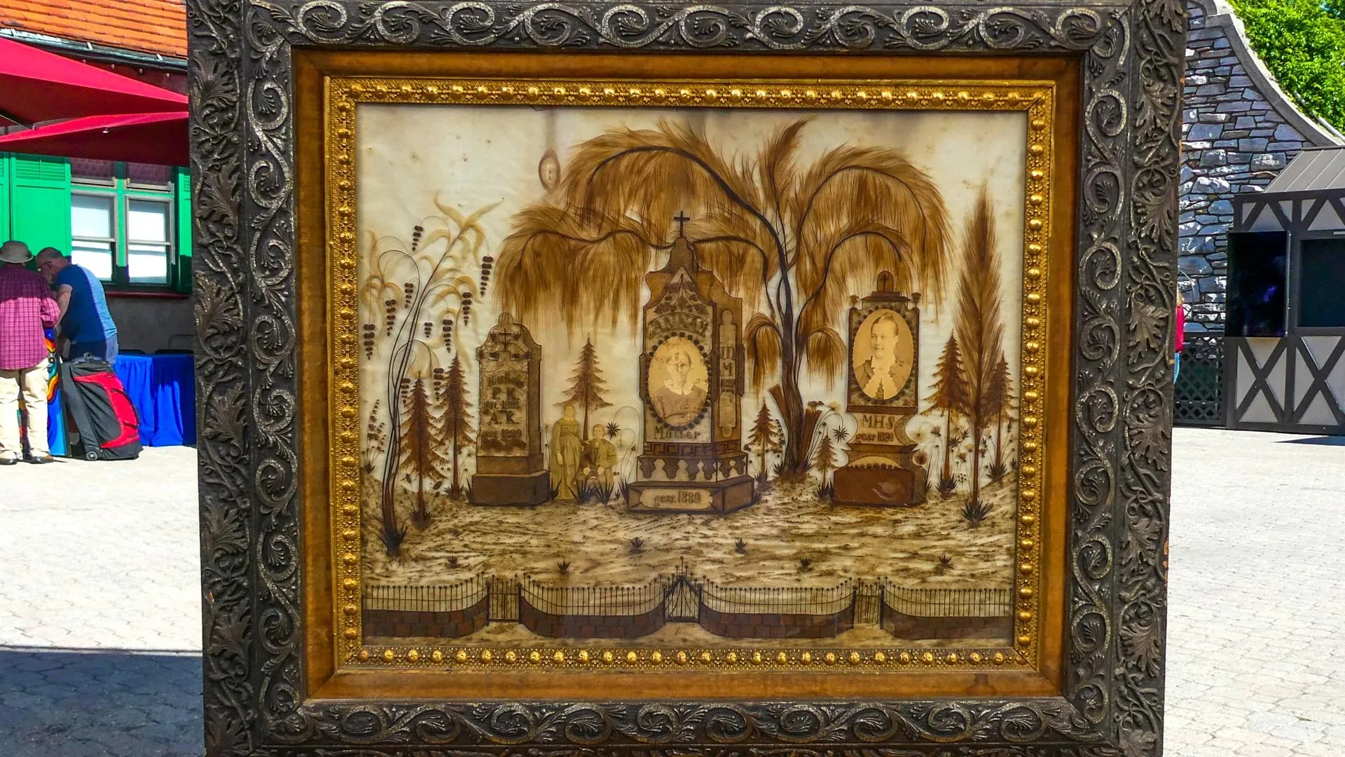 A painting of brown hair depicitng an outdoor fenced landscape in dark metal frame.