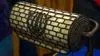 Close up of horizontal cylindrical lamp with pearly white tiles with iron lines outlining a brick like pattern on top.