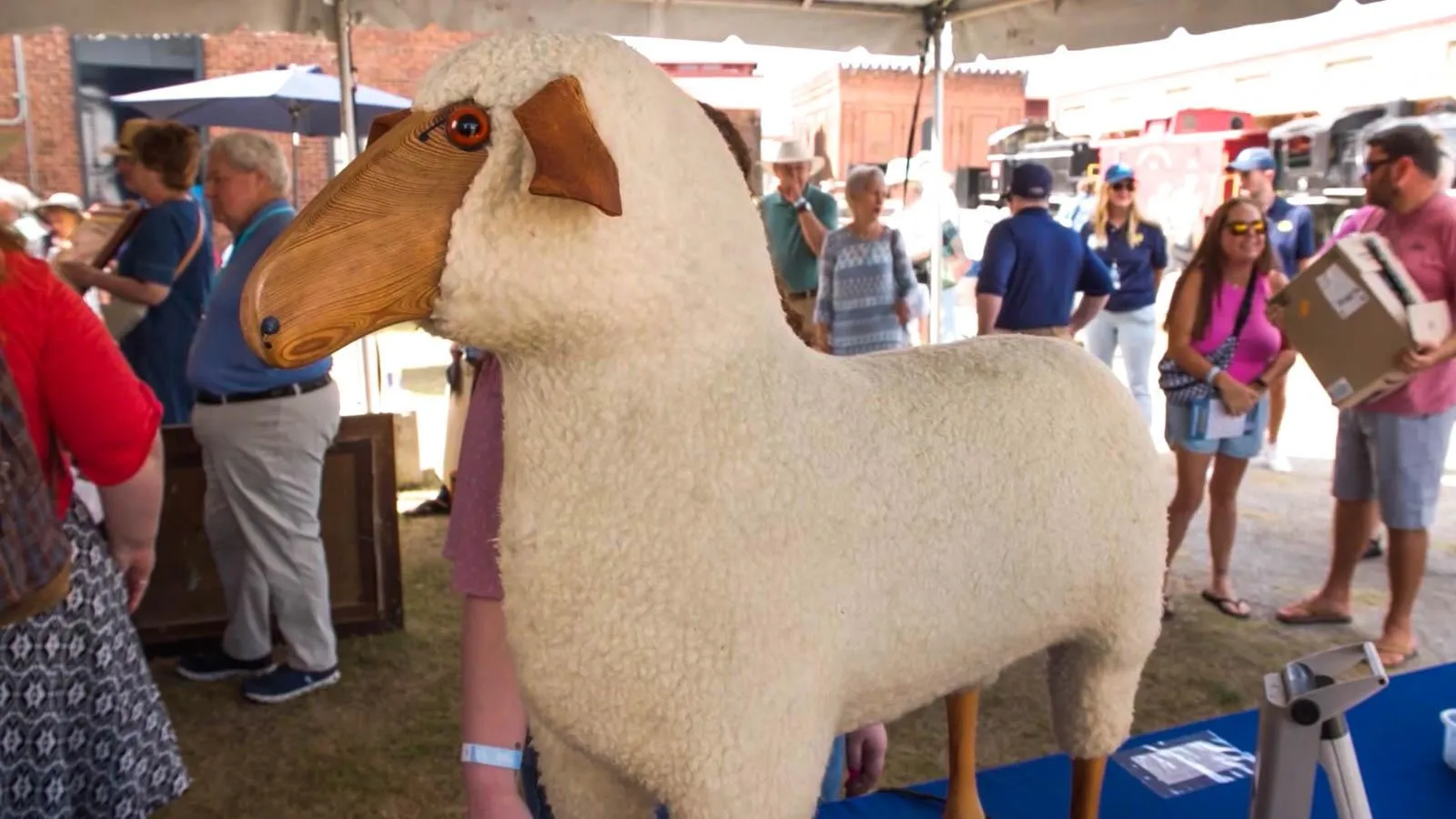 A wooden sheep with white fur stands on top of a table.