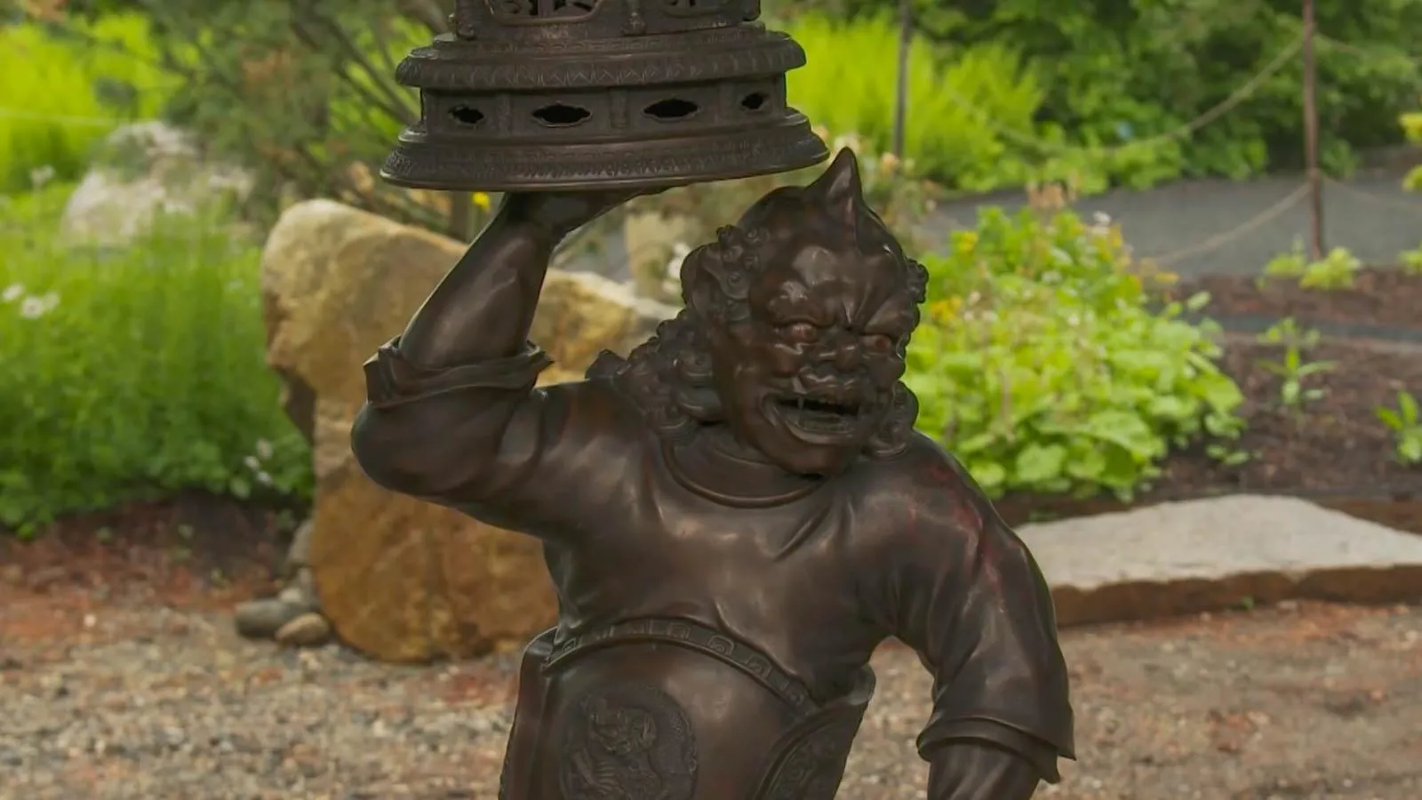 A close up of a demon like bronze figure holding up a bronze circular structure.