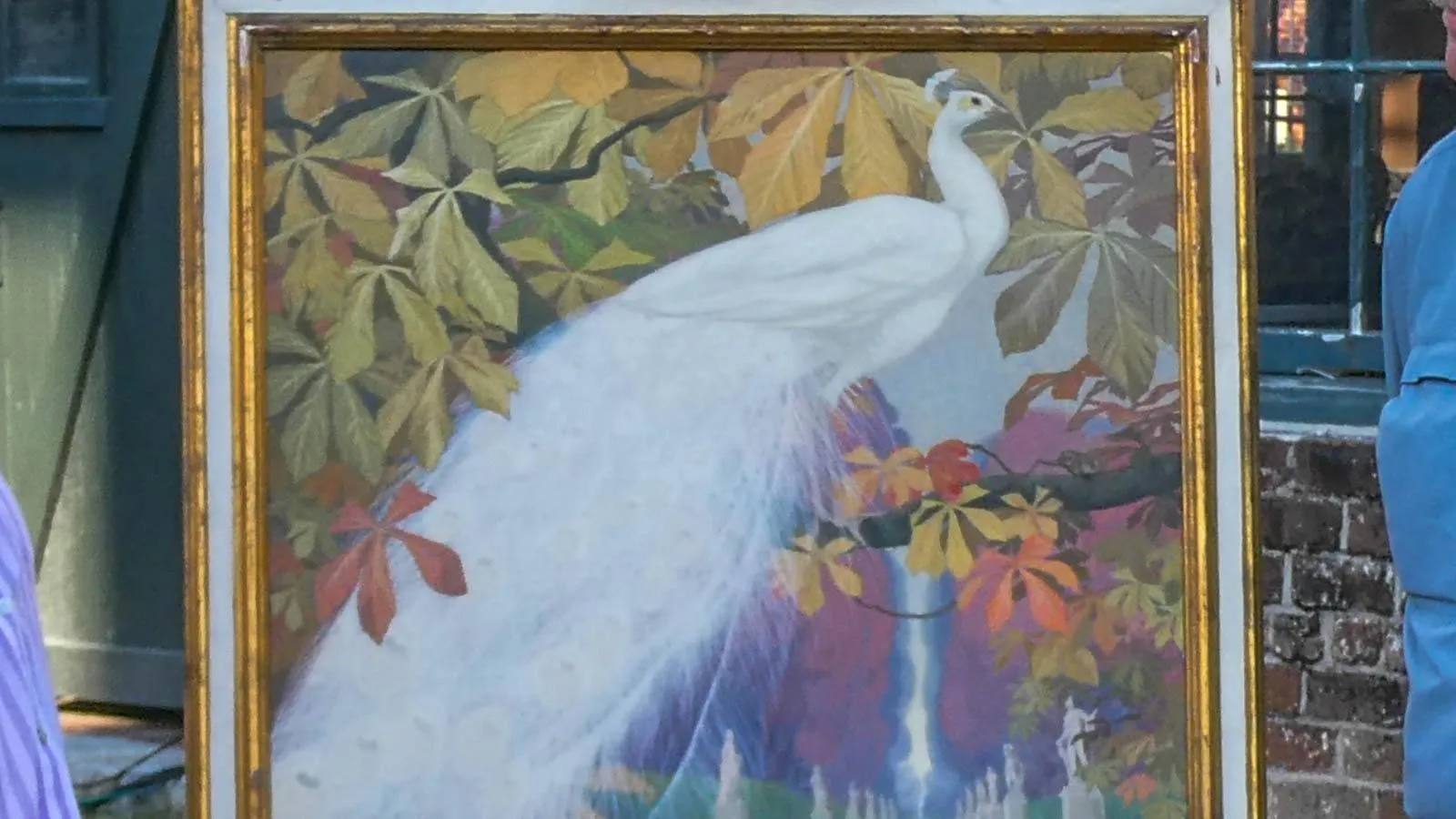 A painting in a gold frame of a white peacock in the center surrounded by multicolored leaves in the foreground and a waterfall in the background.
