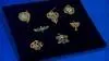 seven pieces of gold jewelry with green accents and nature motifs on black velvet square.