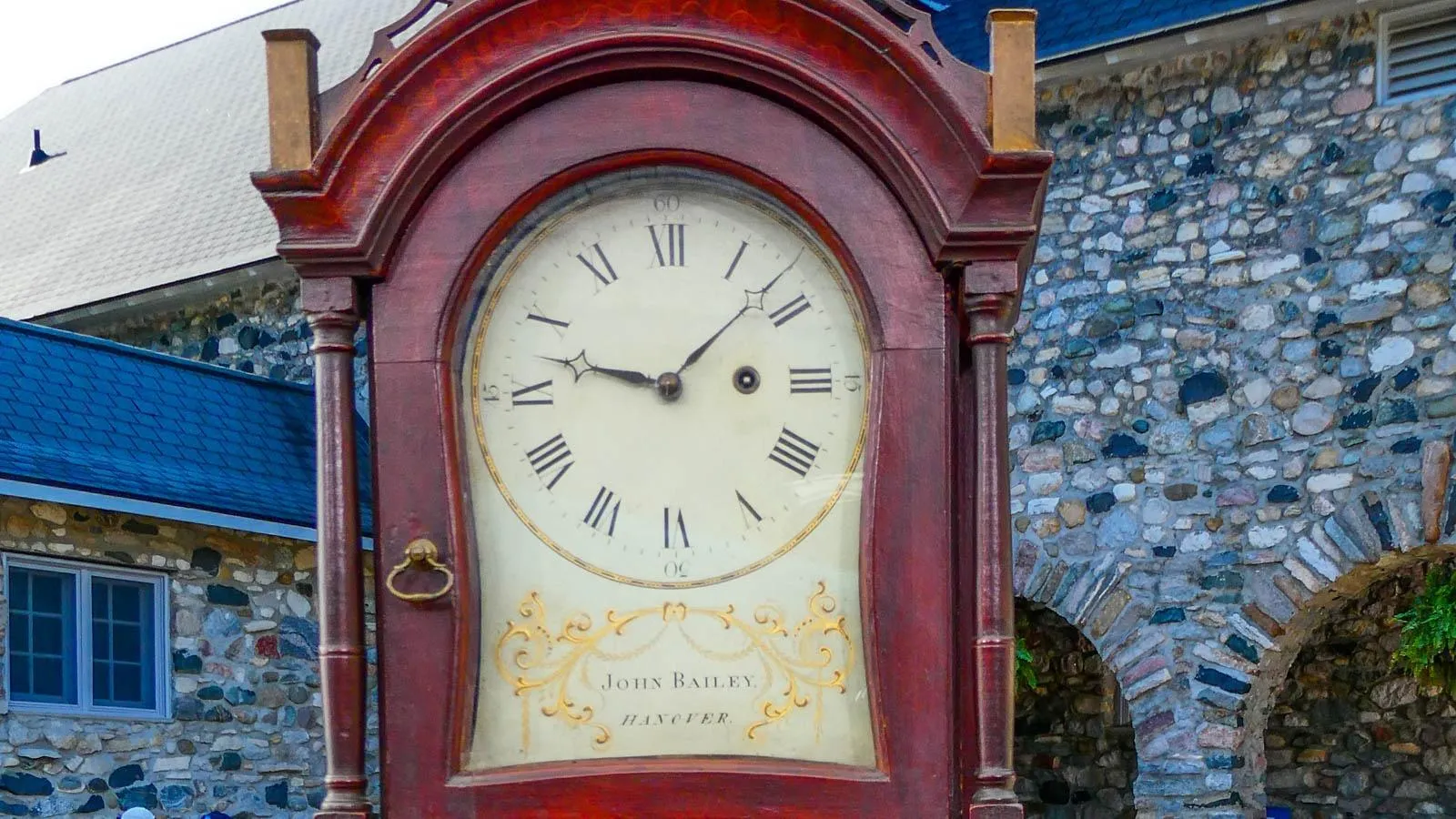 Close up of an older clock made with red colored wood and a cream watchface with serif font.