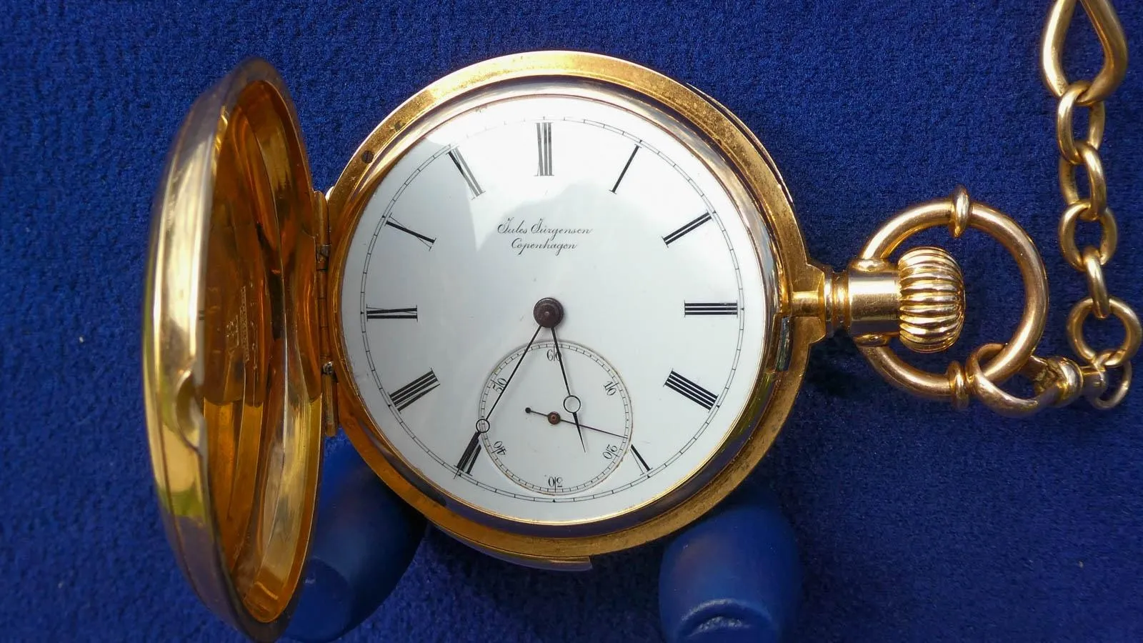 Close up of a gold pocket watch open to its face against a blue background.