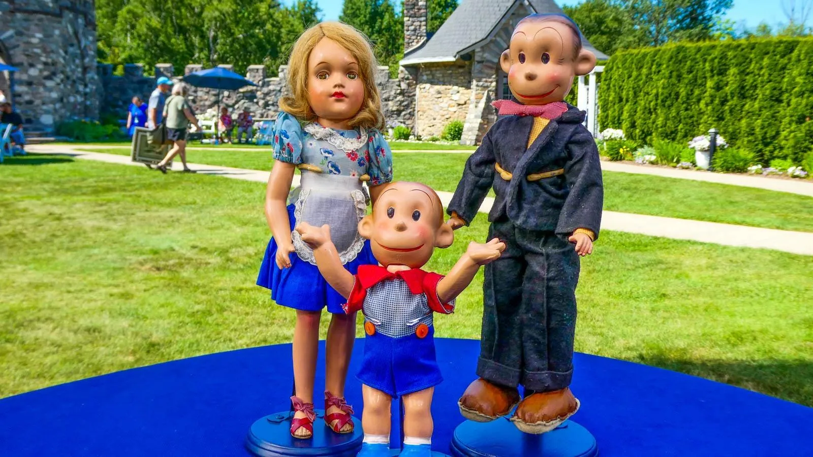 Three dolls mounted on their own display platforms sit on a table together.