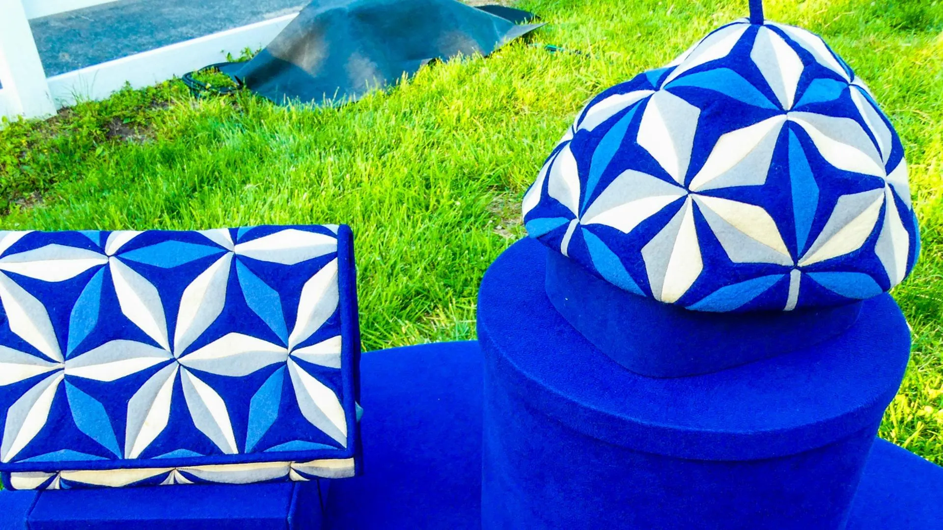 A blue and white paneled clutch and baret sit next to each other on a royal blue table.
