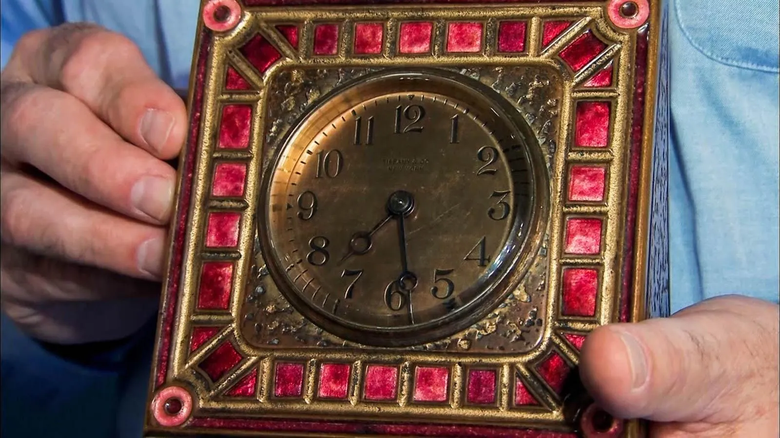 Two hands holding a brass clock with red accents