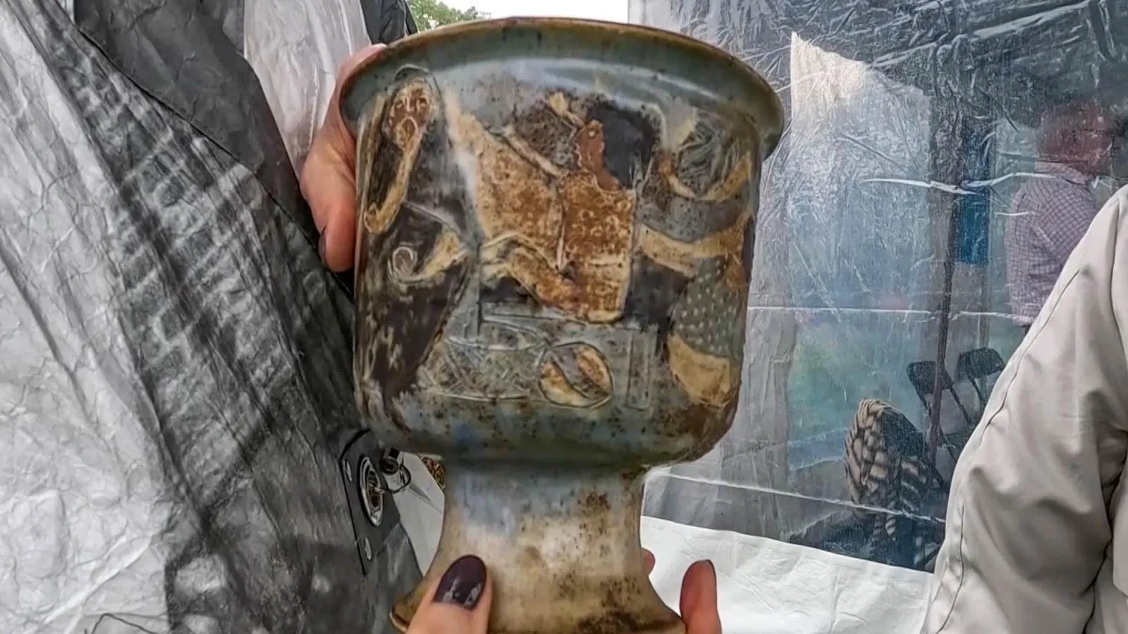 A close up of a speckled vase with person like figured etched into the design.