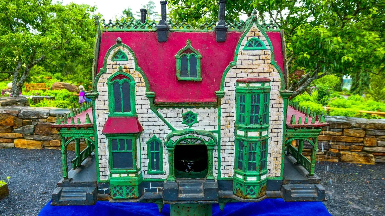 An iron bird house with a red roof, white painted bricked and green accents and outlines.