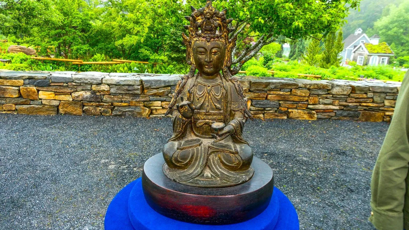 a bronze Guanyin sits on a blue podium in an outdoor enviornment.