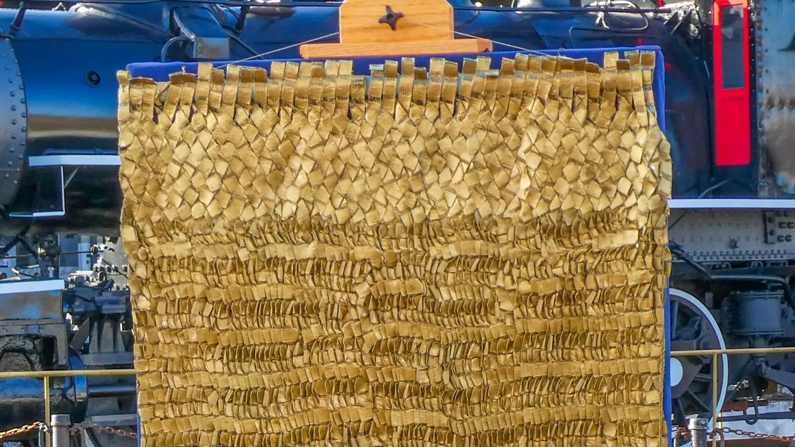 A basket weaved gold tapestry hung up in front of a black train.