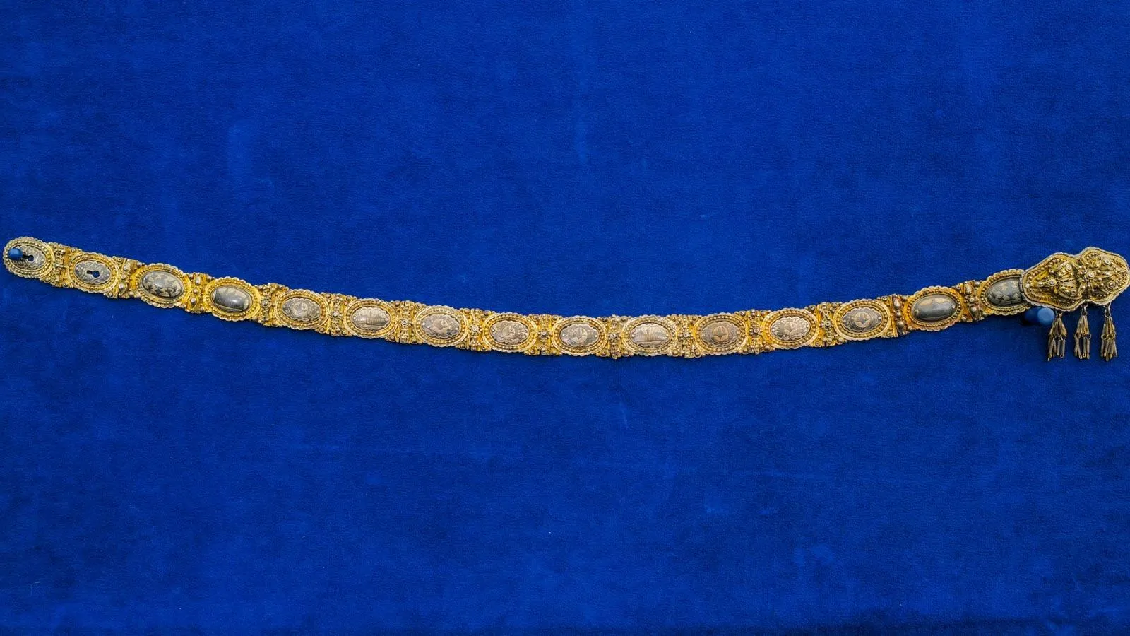 Gold bracelet with thin silver oval details against a royal blue background