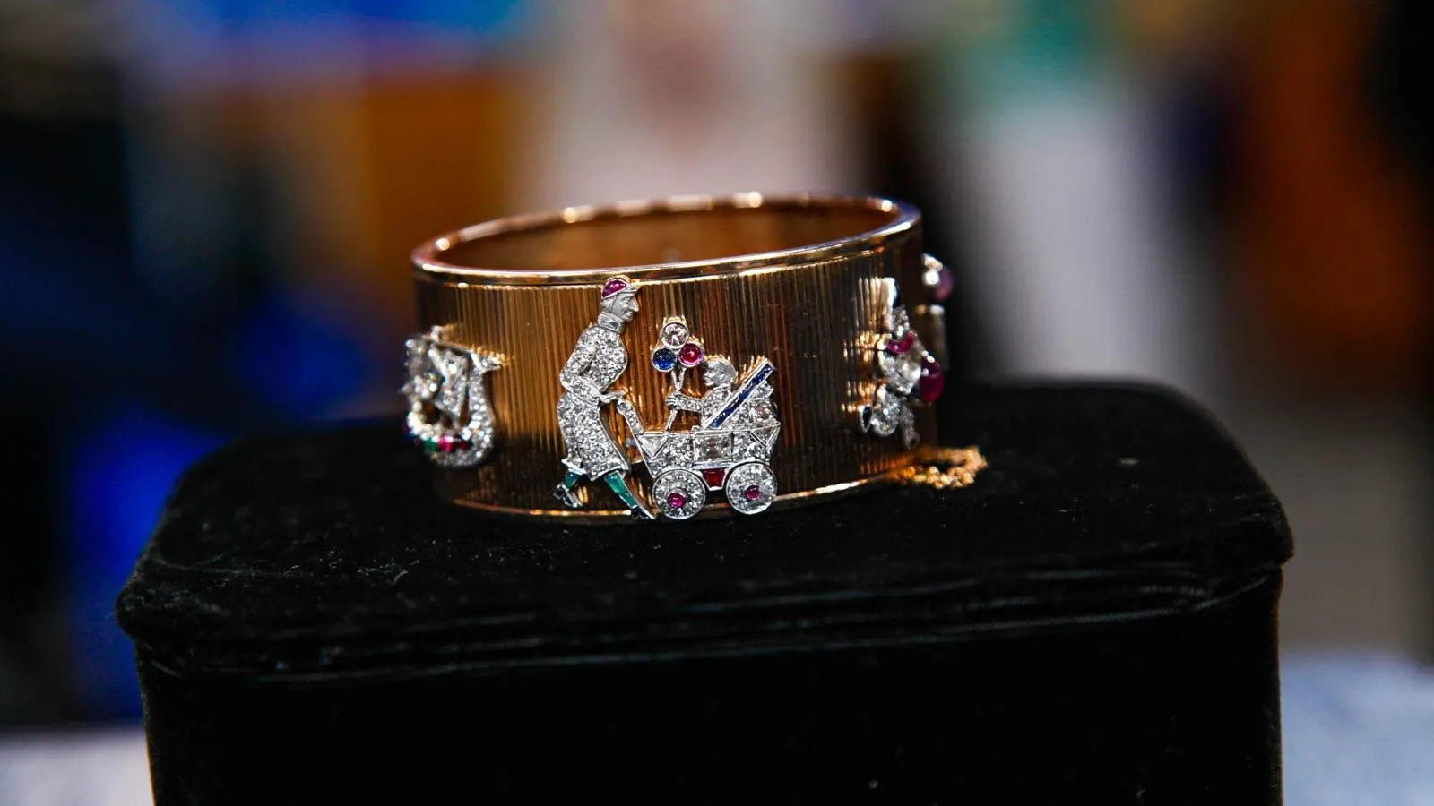 Thick gold bracelet with platinum diamond pictures on the sides, including a woman walking a baby in a stroller.
