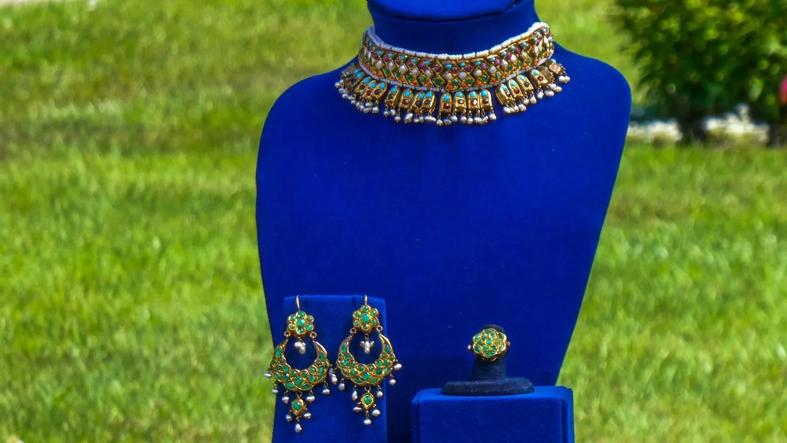 A necklace, set of earrings, and a ring are placed on blue jewelry mounts.