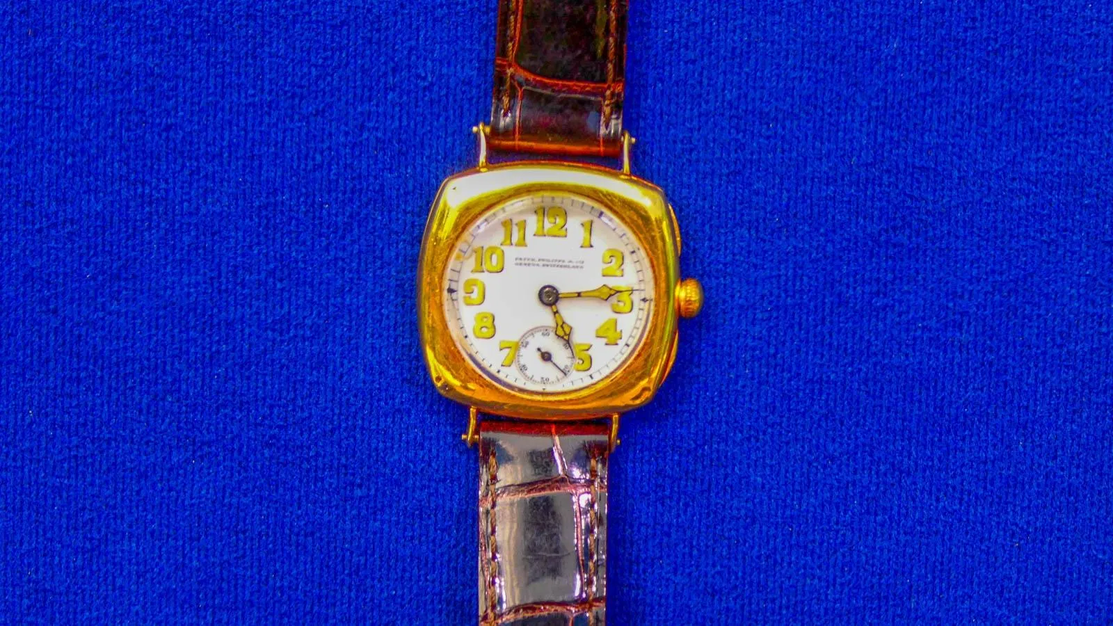 Close on a white watchface with yellow numbers and clock hands. On both sides of the watch face are red leather bands in a crocodile pattern.