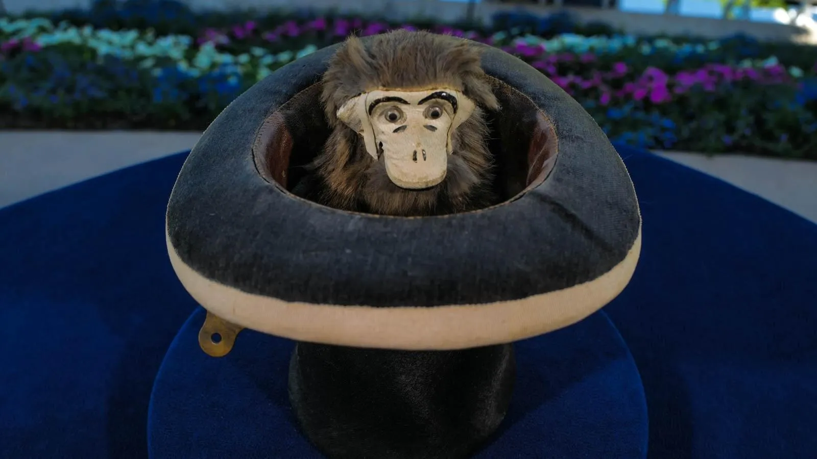 Close up of a mechanical monkey puppet with brown and gray fur sitting in a felted top hat.
