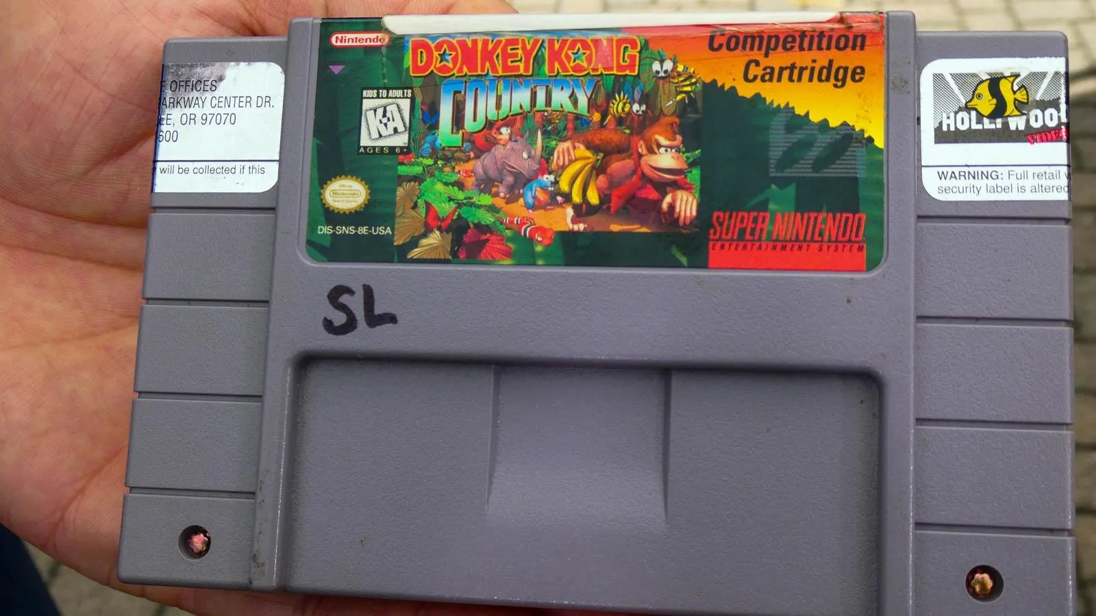 Close up of a hand holding a Nintendo game cartridge for Donkey Kong Country.