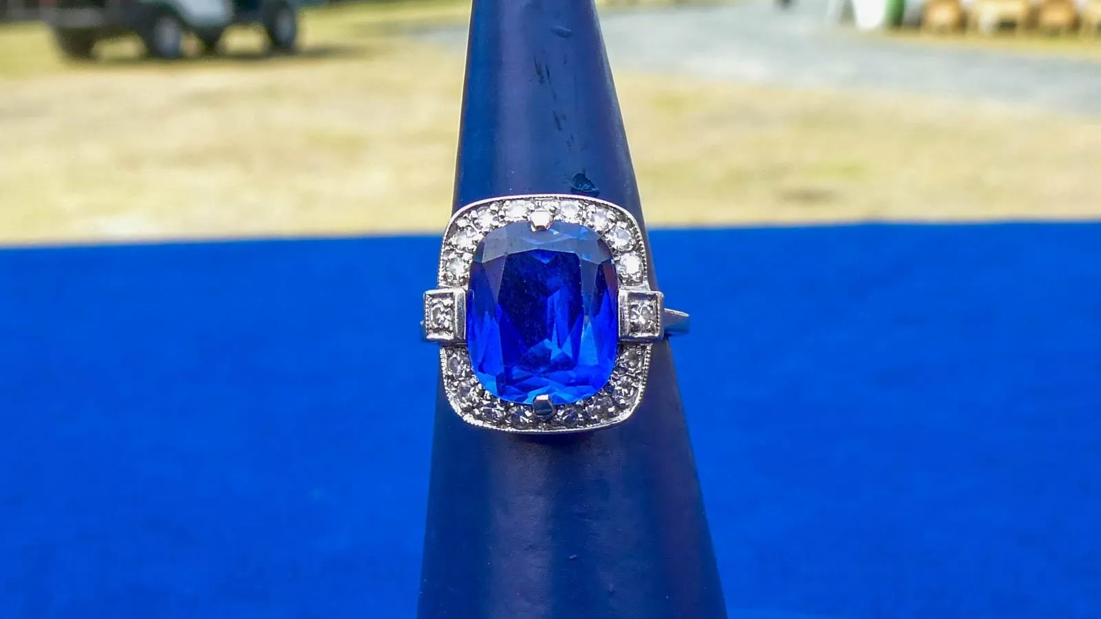 Close up of a ring with a sapphire surrounded by small diamonds sent in a silver band.