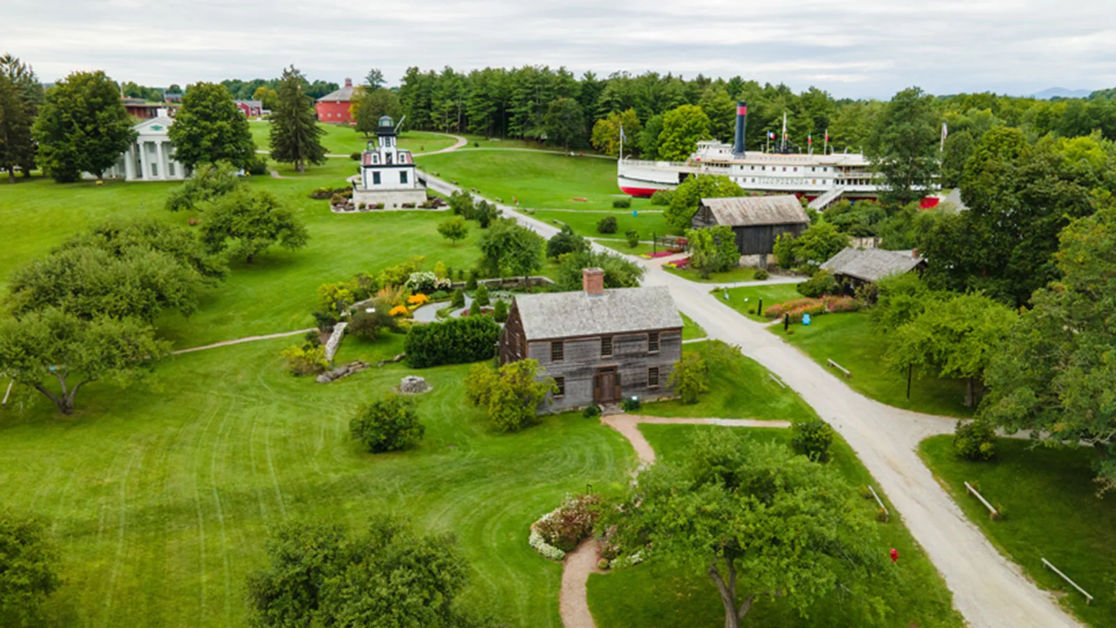 An angled overhead view of a green area with white and brown structures and a boat on display. A brown two-story structure is situated at the center.