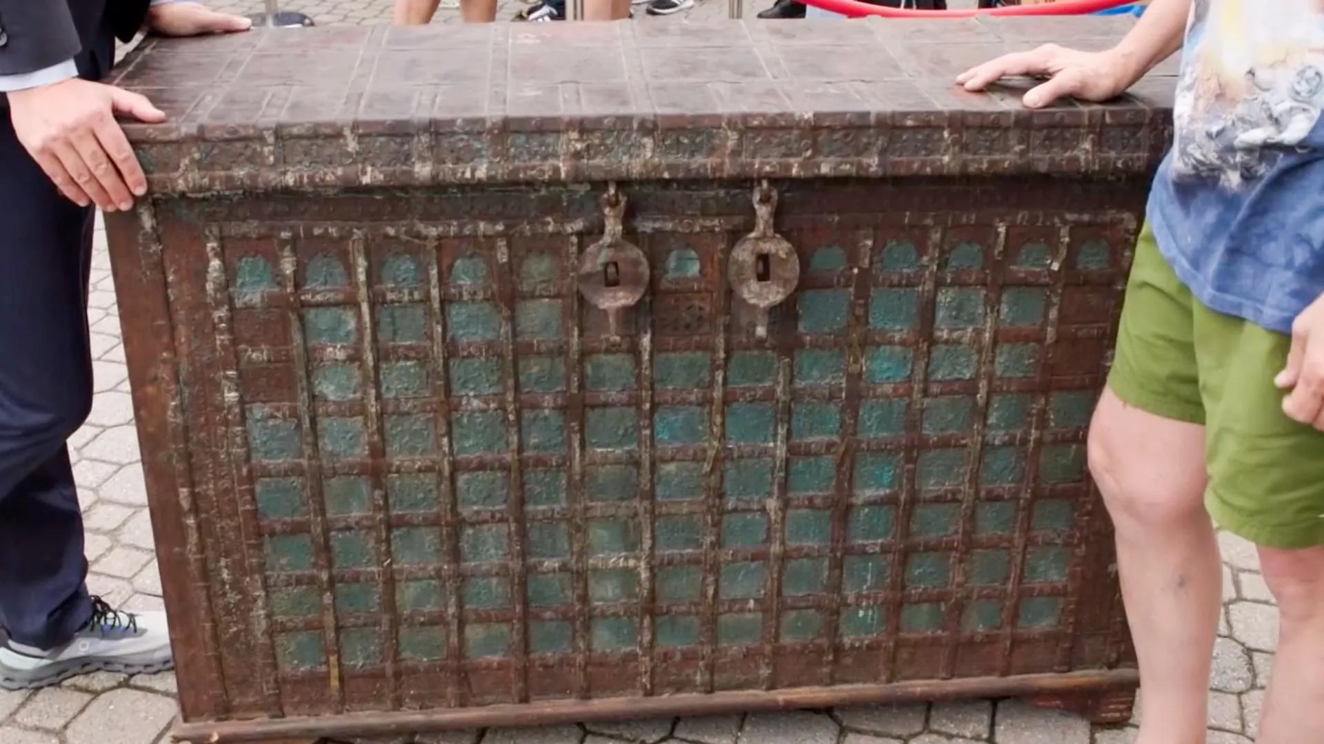 Two people stand on either side of a dark brown and turquoise wood trunk