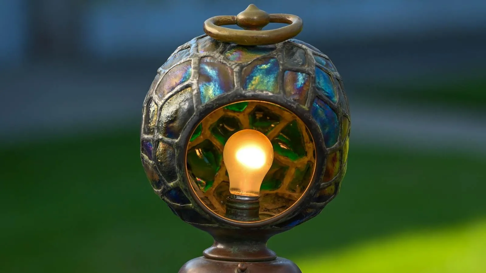 A close up of a round lamp with a turtle shell like pattern in colors of blue and green with a warm toned lightbulb lit up in the center.