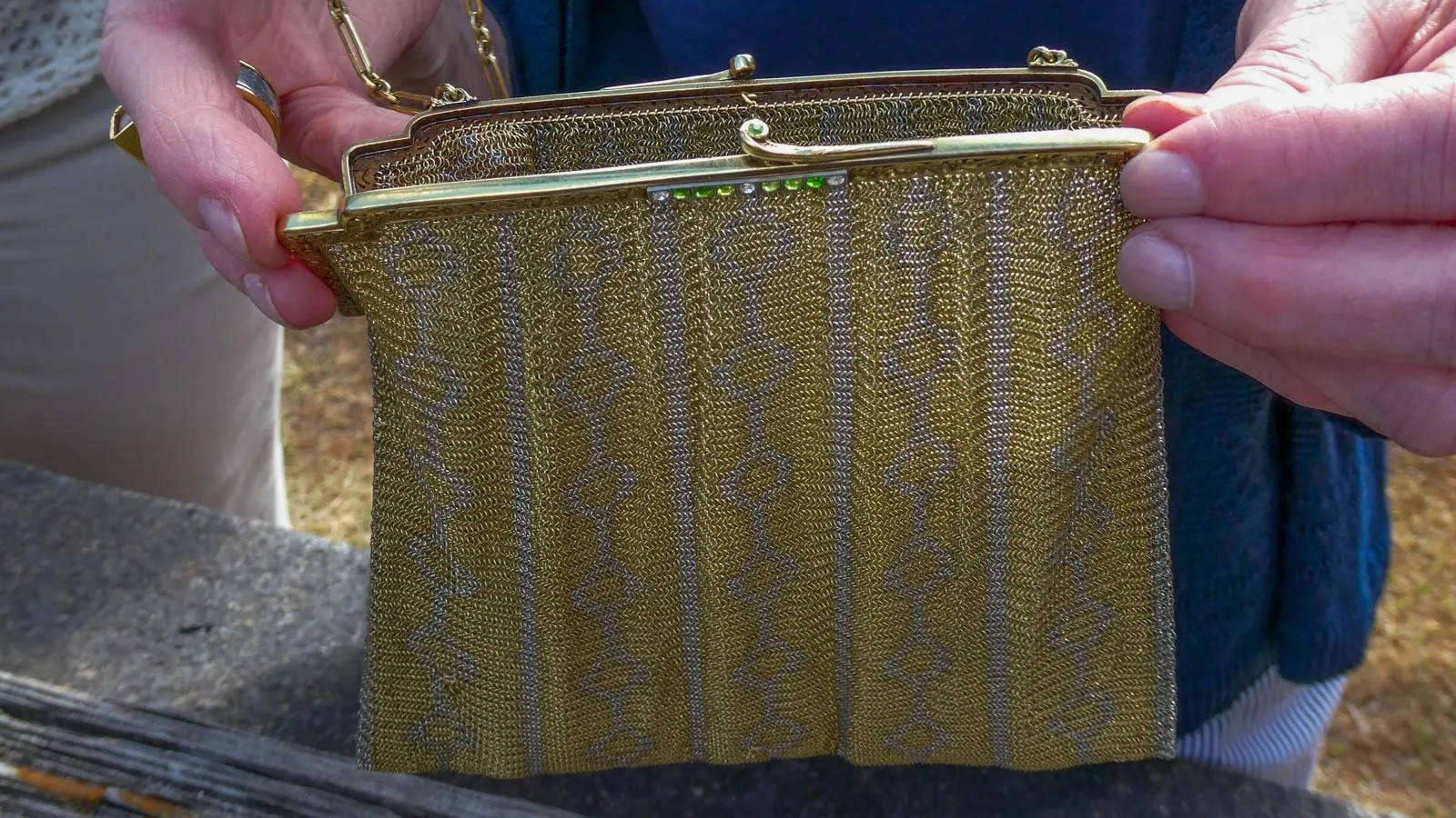 Close up of a square silver and gold chainmail purse with emerald details along the clasp.